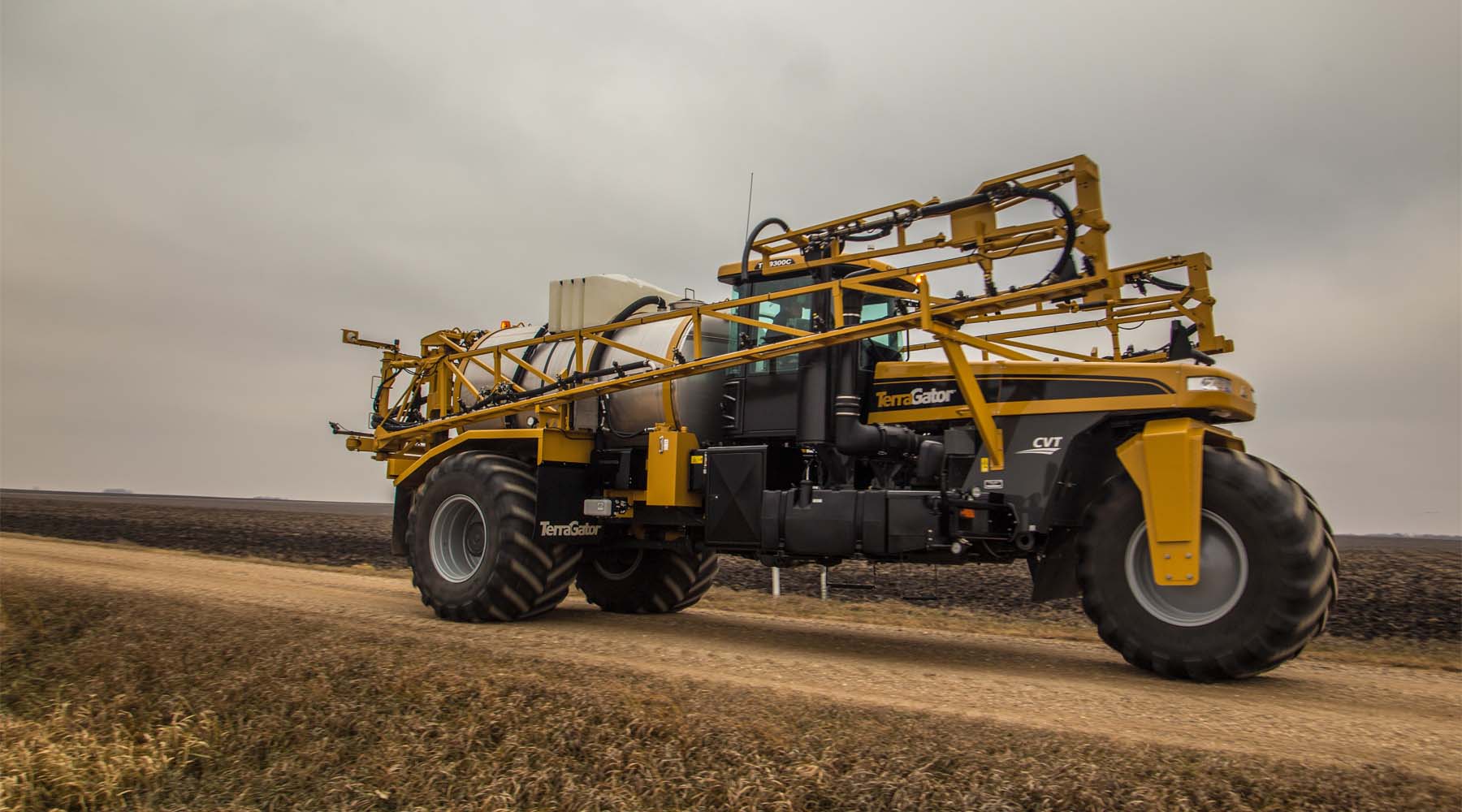 TerraGator C Series CVT applicator with folded boom traveling on farm road between fields under cloudy sky.