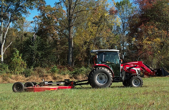 Side profile of Massey Ferguson 2M Series compact tractor towing a rotary cutter through a grassy field, emphasizing durability and high-efficiency mowing capabilities.
