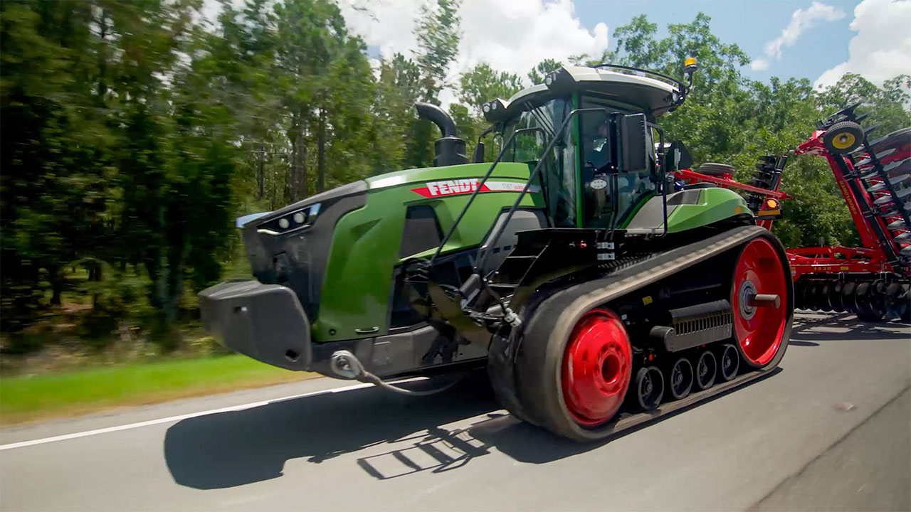 Fendt 1100 Vario MT tracked tractor towing red tillage equipment on highway, built for power, transport efficiency, and field readiness.