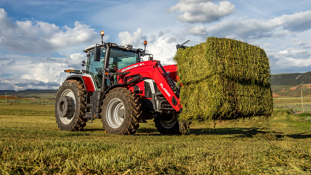 Massey Ferguson 8S Series tractor lifting hay bales in a field, ideal for heavy-duty hay and forage operations.