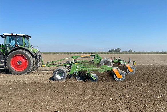 Fendt tractor pulling an Amazone Catros+ 9003-2TX compact disc harrow through a freshly plowed field under clear blue skies.