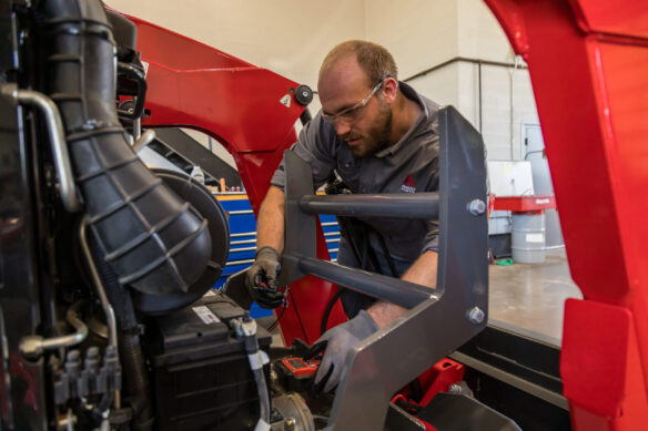 Service technician performing maintenance on the front of a Massey Ferguson.