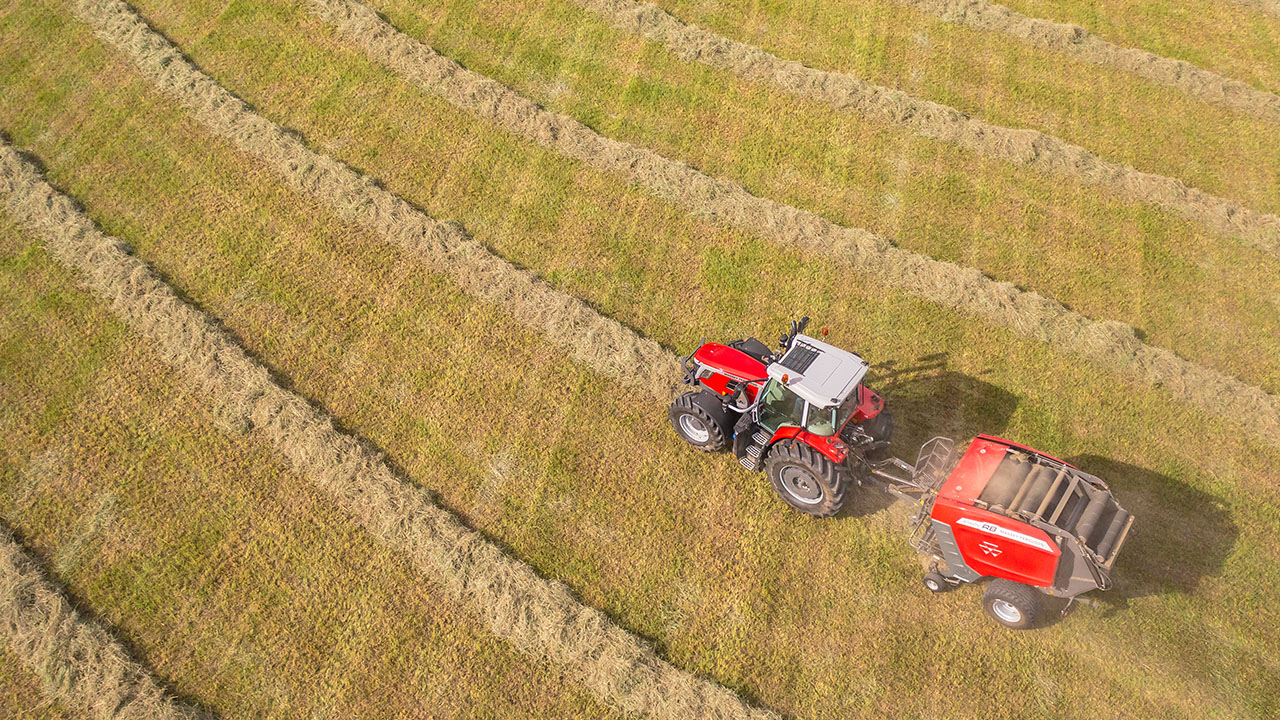 Aerial view of Hesston by Massey Ferguson RB Series round baler and tractor harvesting hay in rows, producing consistent round bales.