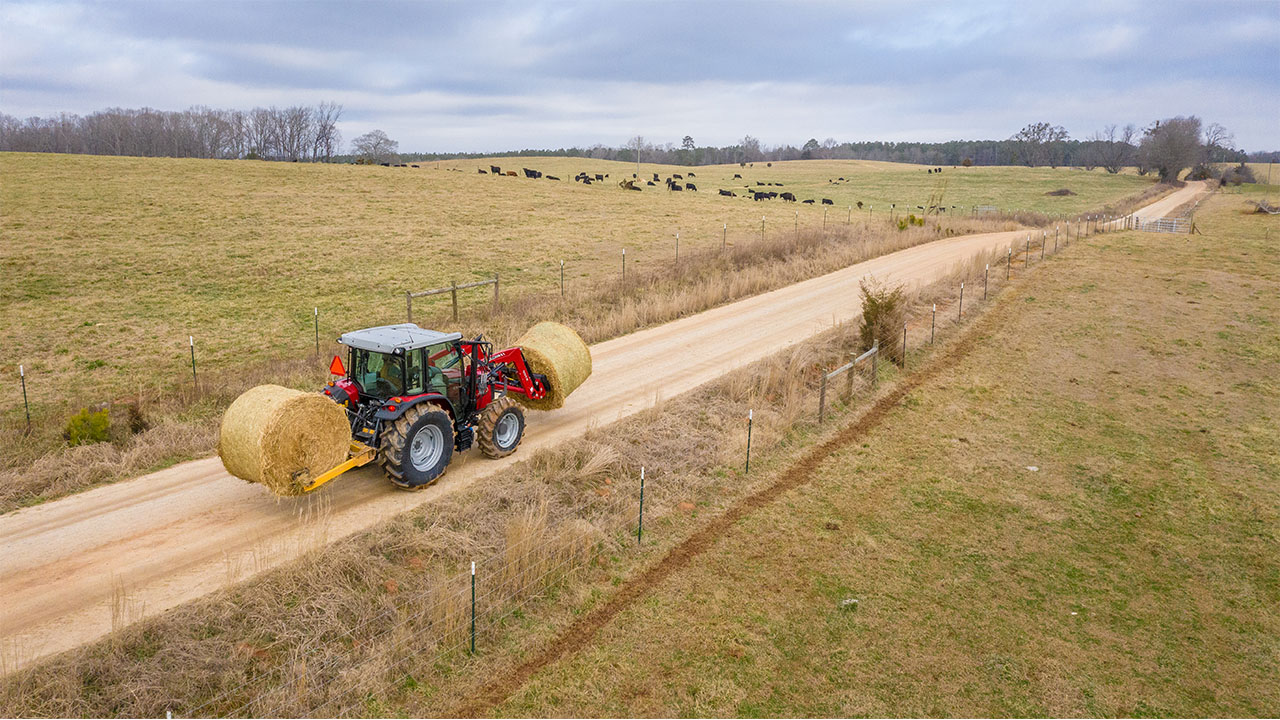 Massey Ferguson 4700 Series tractor lifting large round hay bale, ideal for livestock and heavy-duty farm operations.