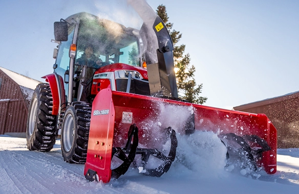 Massey Ferguson 1M Series compact tractor equipped with a rear snow blower, actively clearing snow on a residential property.