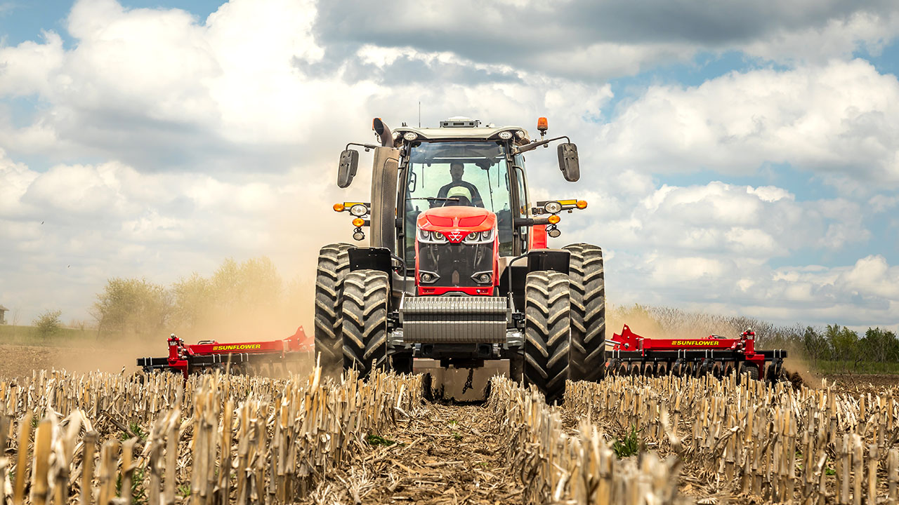 Massey Ferguson 8700S Series tractor pulling Sunflower tillage equipment across a harvested field during golden hour.
