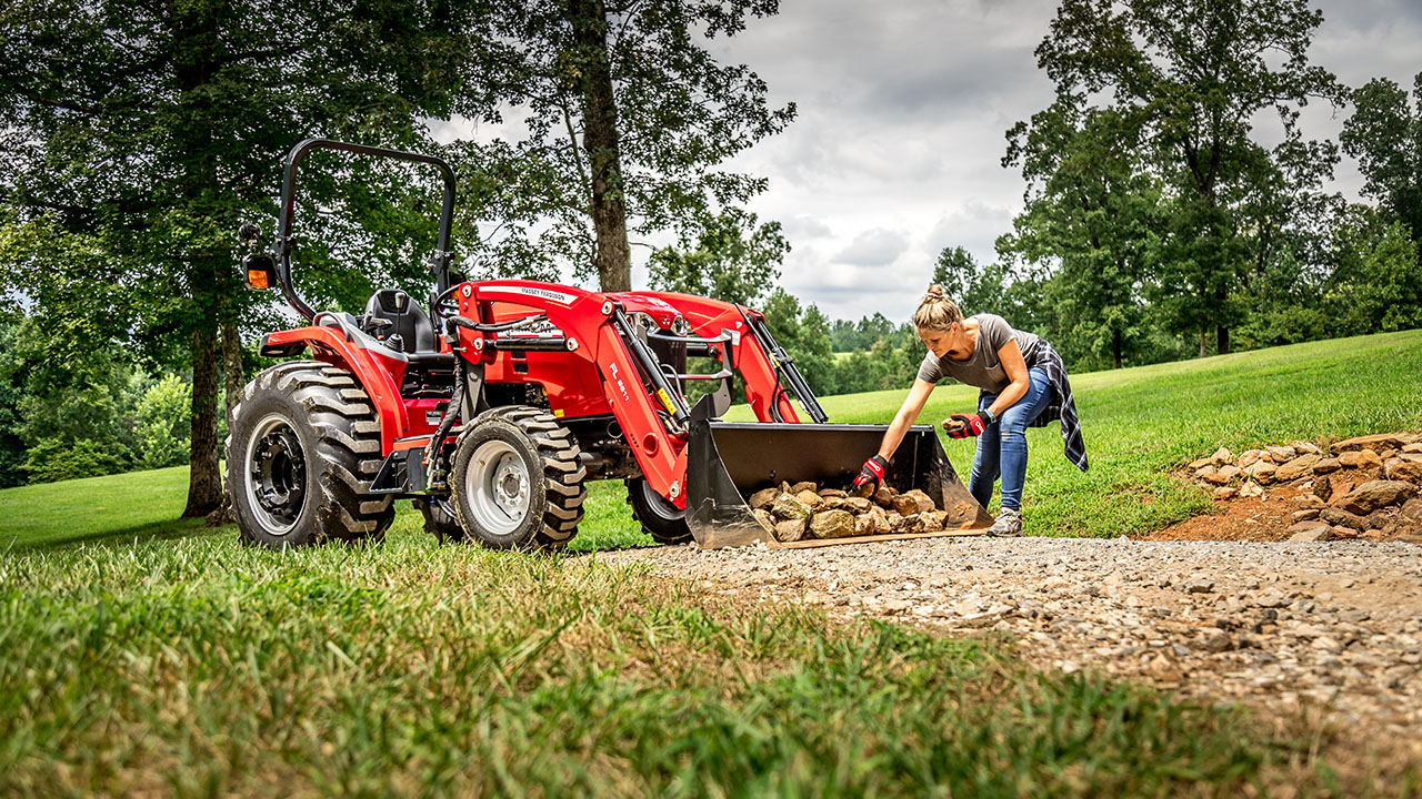 Woman unloading rocks from Massey Ferguson 1800M compact tractor with front loader, ideal for landscaping and property maintenance.