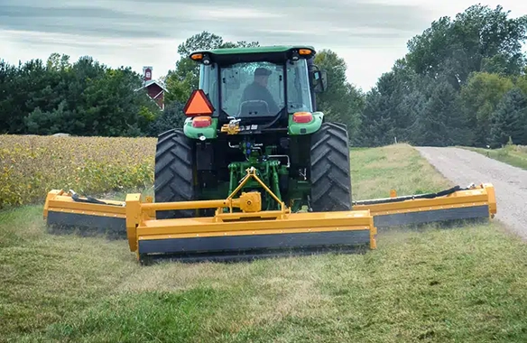 Diamond Mowers flail mower system mounted on a green tractor, mowing grass along a rural roadside with precision and wide coverage.