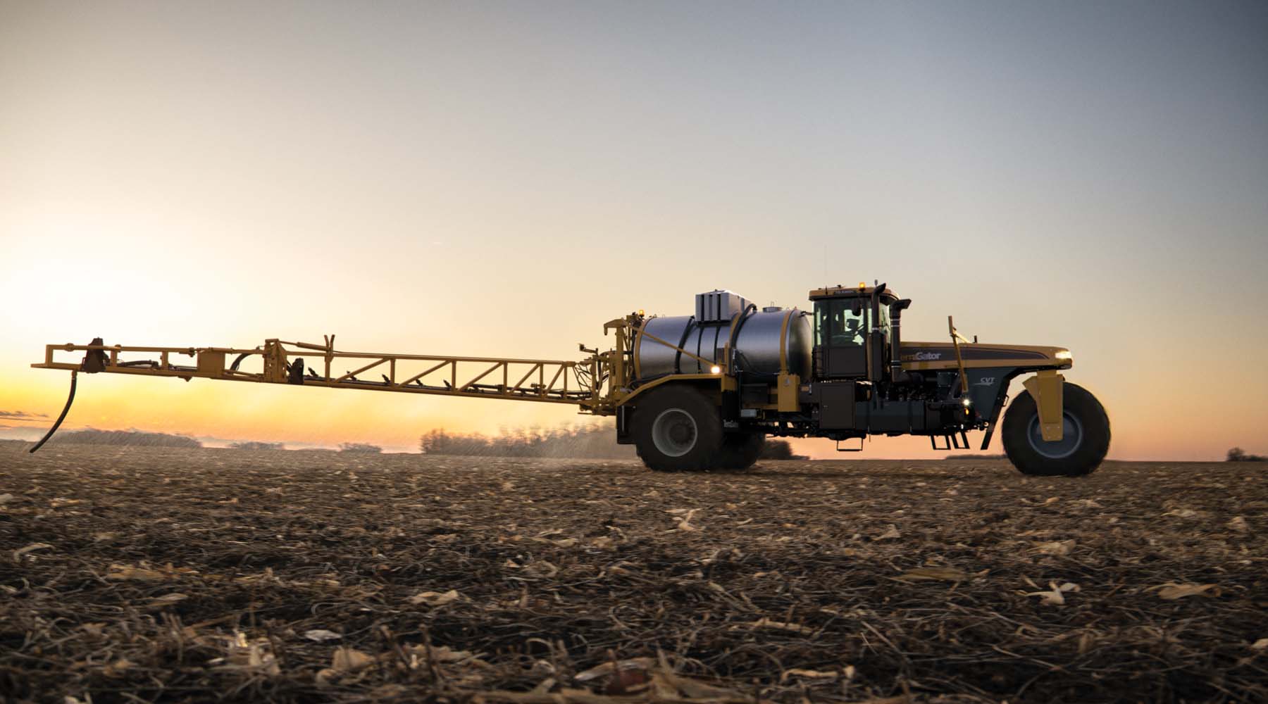 TerraGator C Series high-clearance applicator spraying field at sunset with extended boom arm.