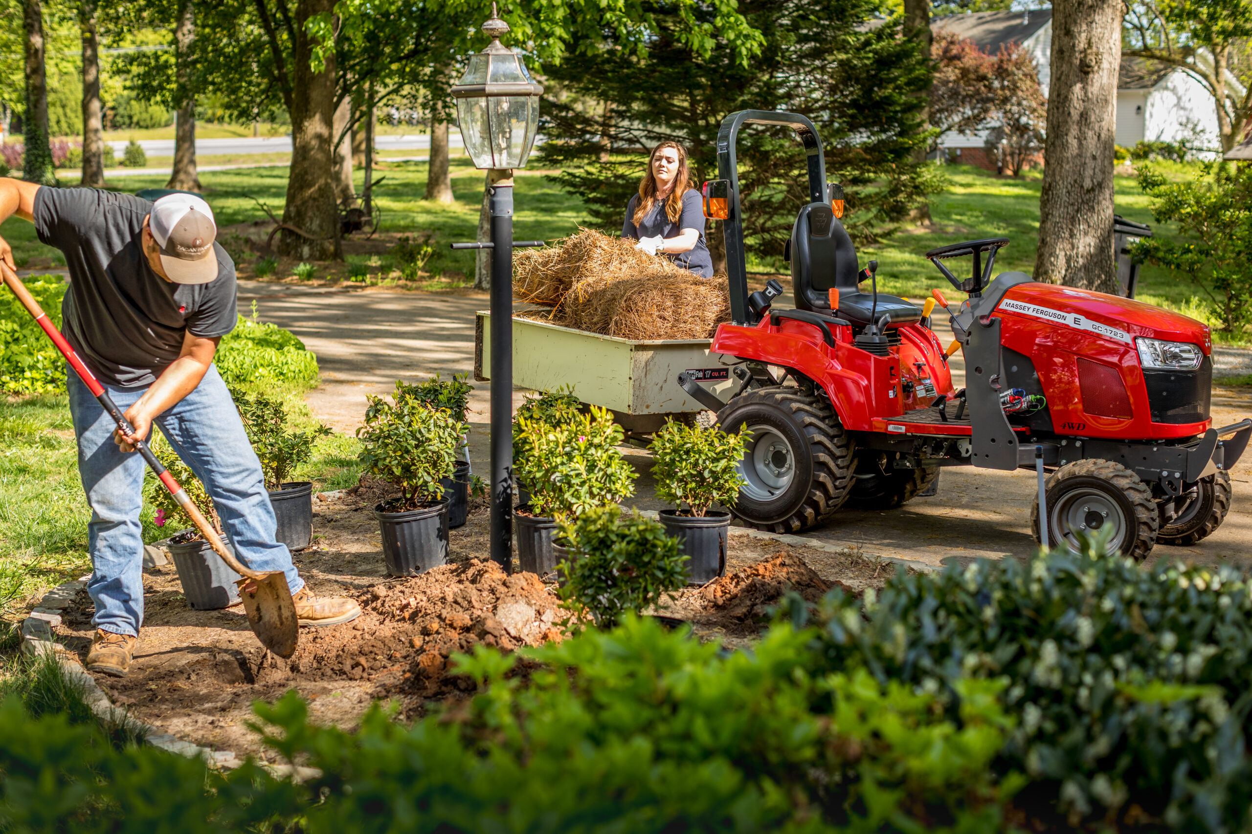 A Massey Ferguson GC1700 Series sub-compact tractor towing a small tractor of landscaping mulch.