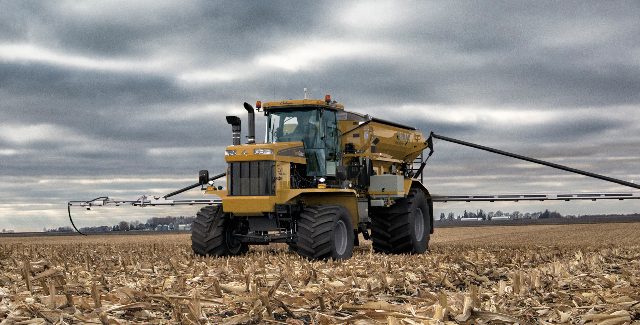 TerraGator 8400 C Series applicator spreading dry fertilizer over harvested cornfield under cloudy sky.