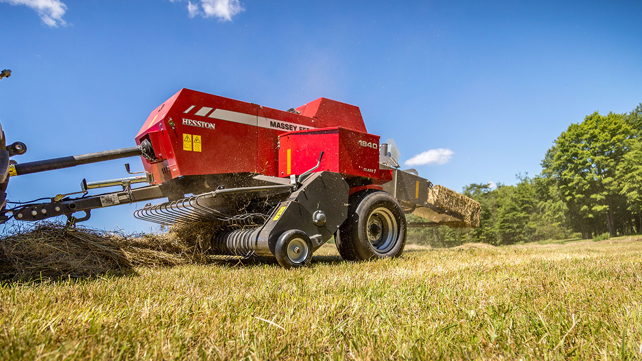 Hesston by Massey Ferguson 1840 small square baler efficiently picking up and forming tight hay bales in a grassy field.