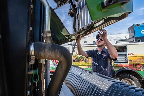 AgRevolution service technician performing maintenance on agricultural equipment outdoors.