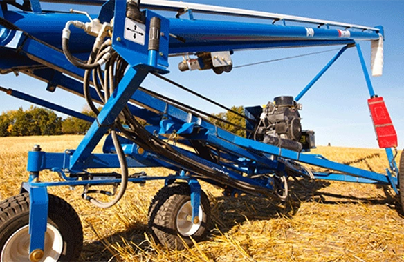 Close-up view of a Brandt EZMover auger mover system in a harvested field, showcasing hydraulic components and mobility for easy auger positioning.