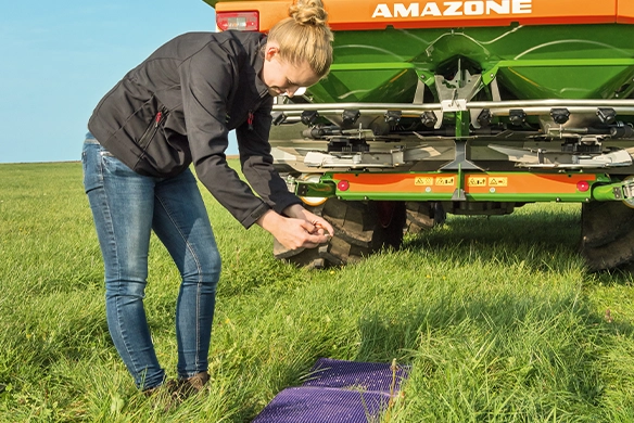 Farmer using Amazone EasyCheck mats behind a ZA-TS spreader to verify fertilizer distribution accuracy in the field.