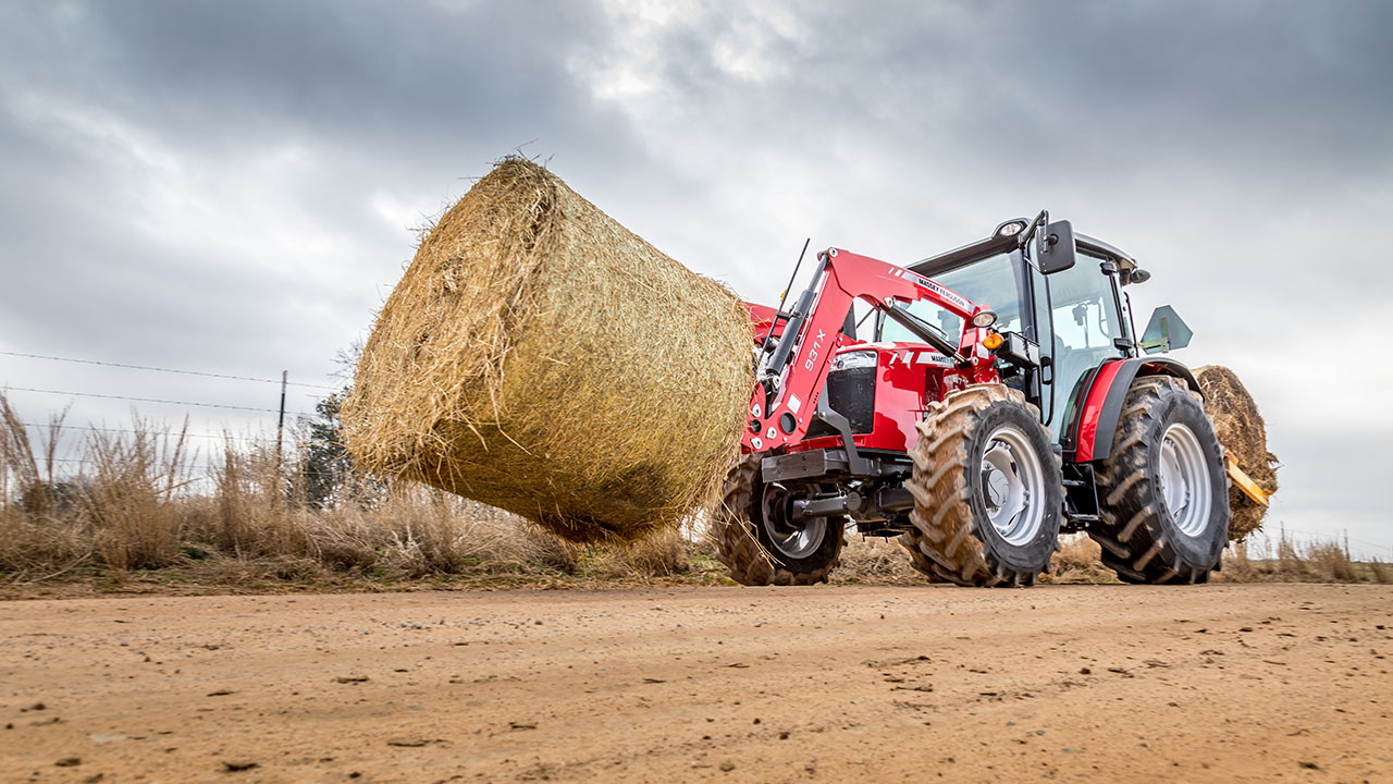Massey Ferguson 4700 Series tractor lifting large round hay bale, ideal for livestock and heavy-duty farm operations.