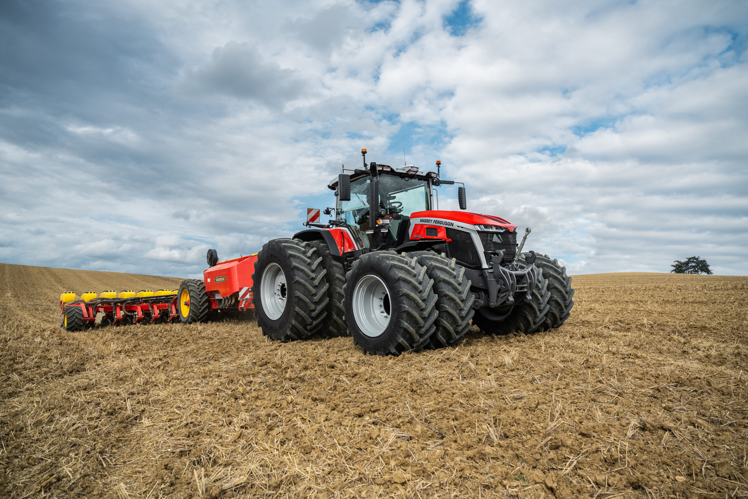 Massey Ferguson 9S Series tractor working in a harvested field with tillage equipment in rolling countryside terrain.