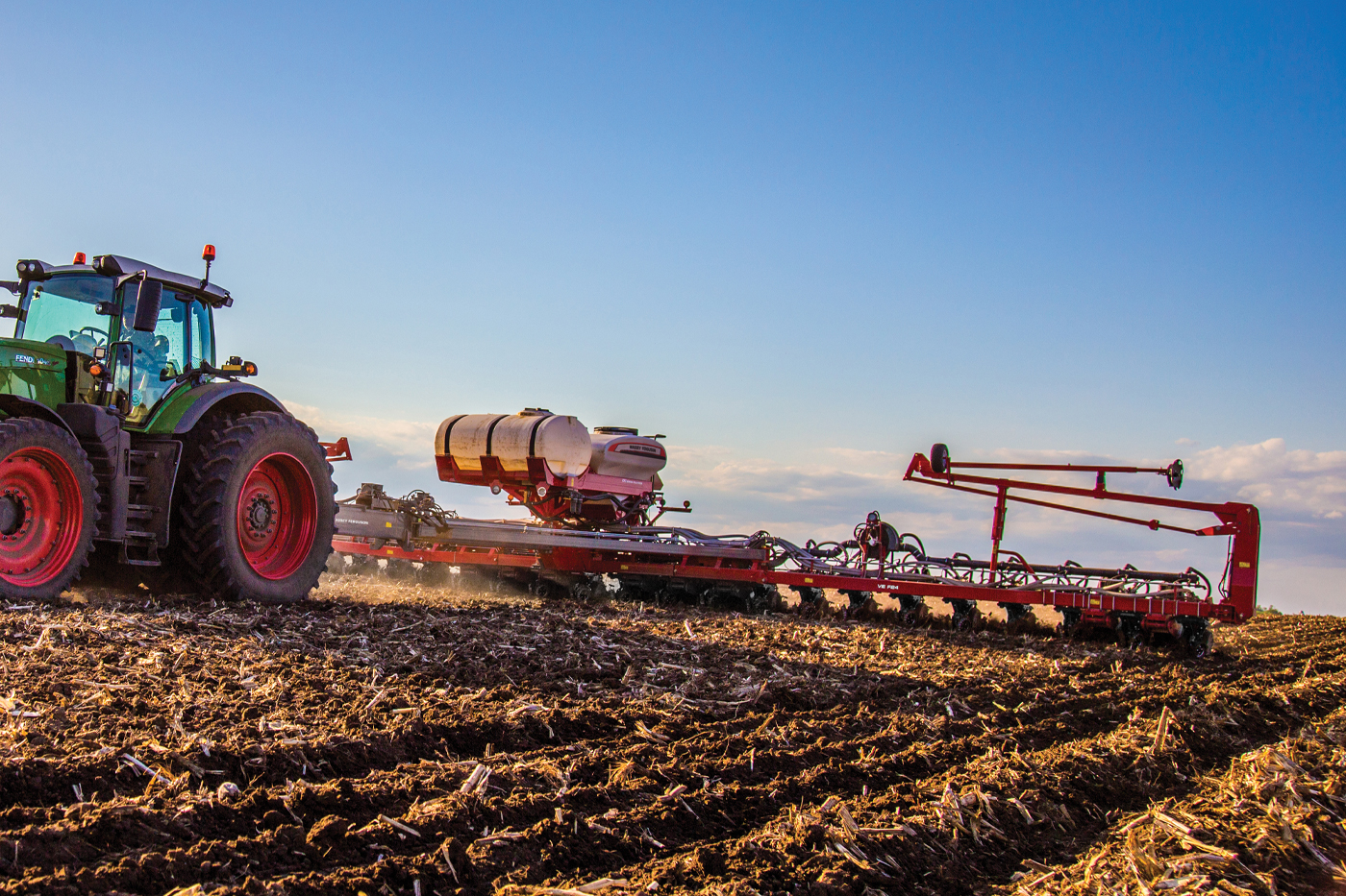 Fendt tractor towing Massey Ferguson planter across field during spring planting, showcasing AGCO precision farming equipment.