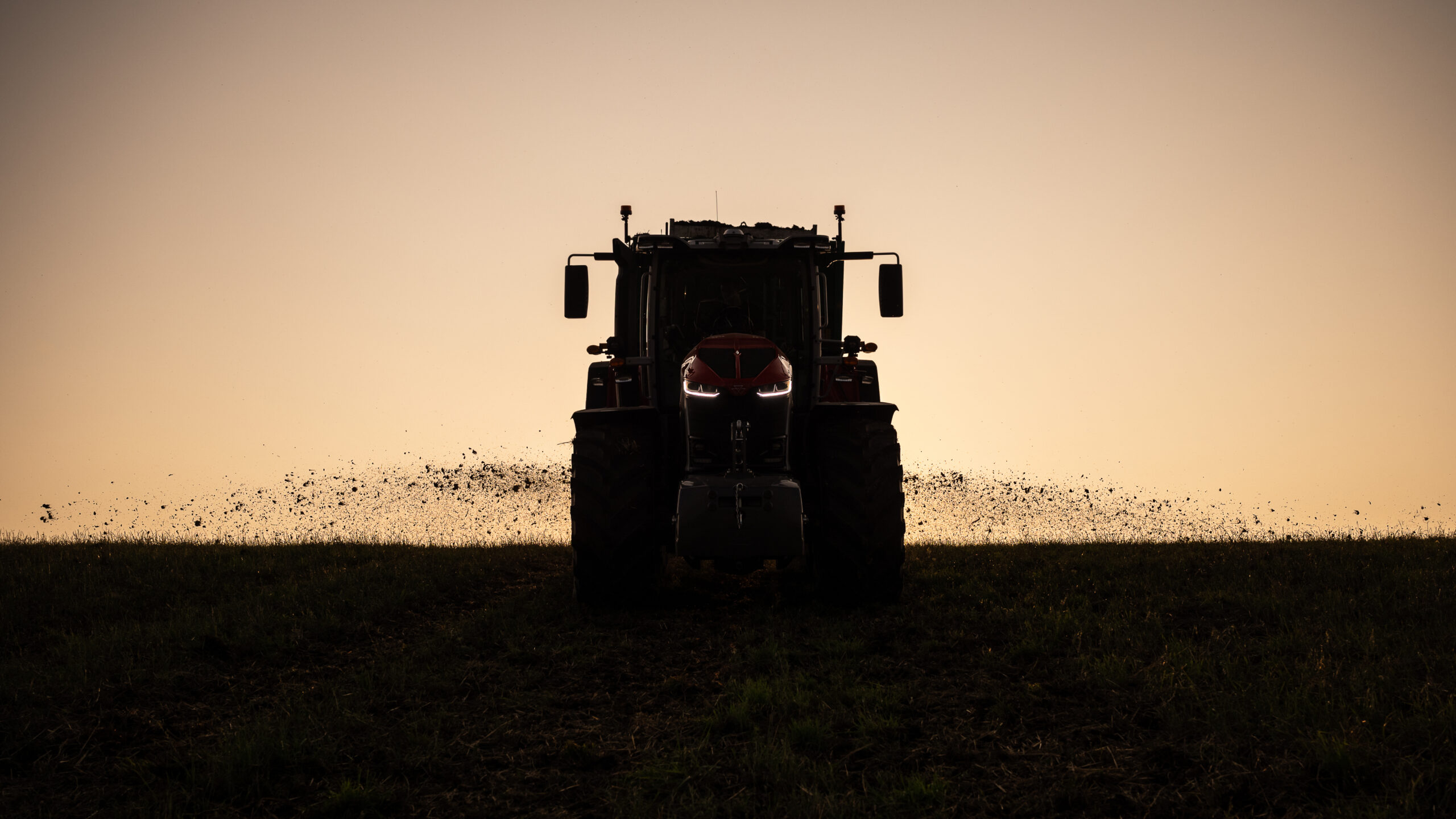 Massey Ferguson 9S Series tractor at dusk with LED headlights on, working in the field and kicking up soil.