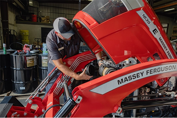 Service technician changing a filter under the hood of a Massey Ferguson tractor.