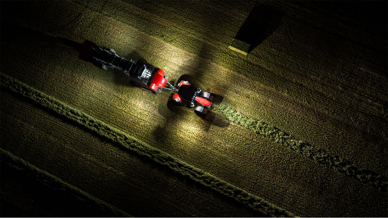 Hesston by Massey Ferguson LB2200 Series baler operating at night, illuminated by tractor lights in a freshly cut hayfield.