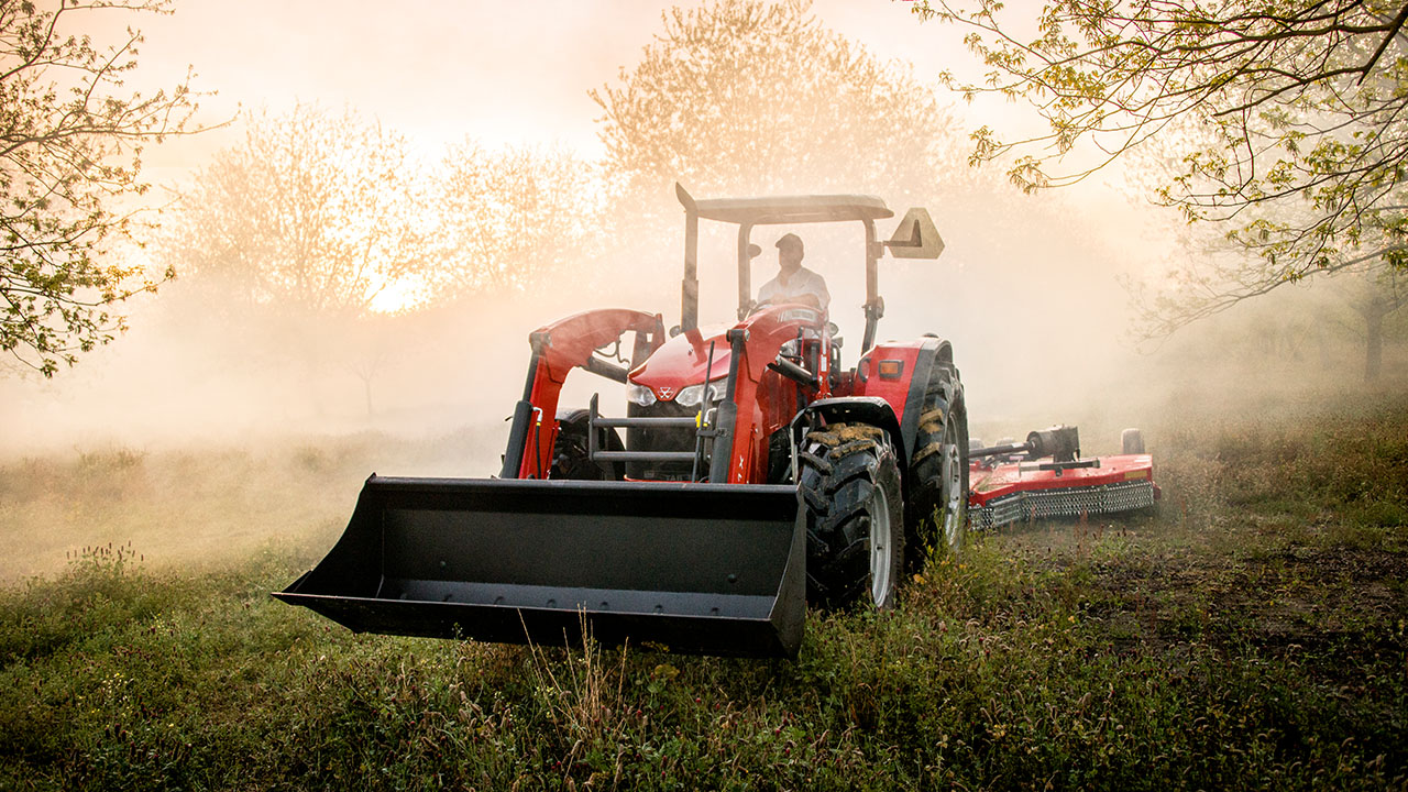 Massey Ferguson 5700 Series tractor with loader and rotary cutter working at sunrise, ideal for land clearing and farm maintenance.