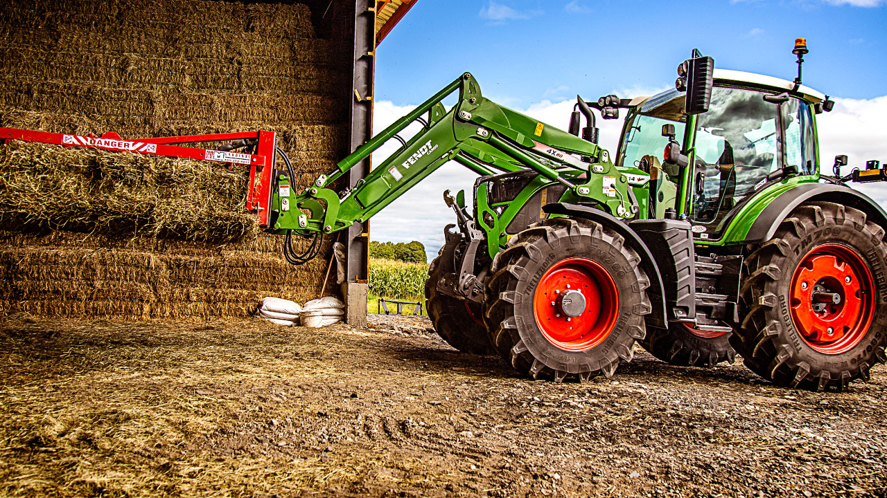 Fendt 500 Vario tractor stacking hay bales using bale spear attachment on a farm, showcasing AGCO equipment.