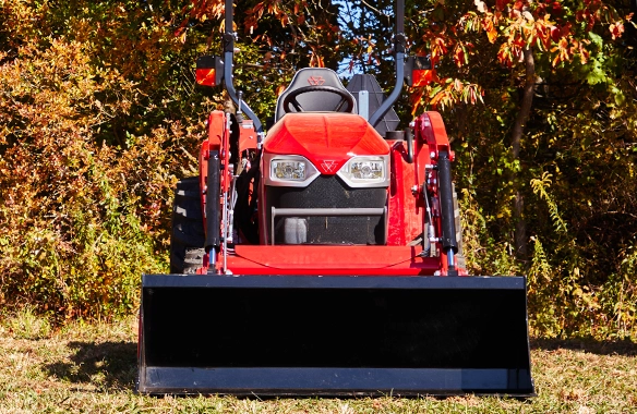 Front view of a Massey Ferguson 2E Series compact tractor with front-end loader parked on grass, showcasing the rugged front grill and compact utility design ideal for residential and agricultural work.