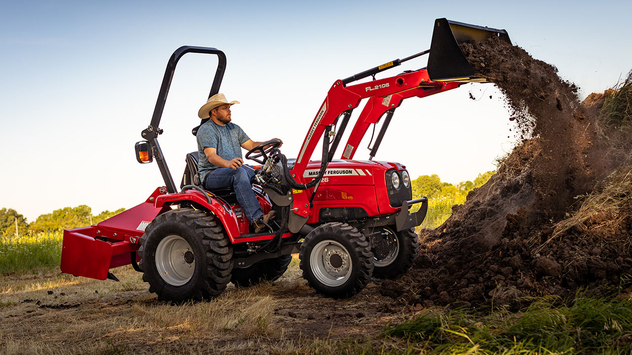 Man operating Massey Ferguson 1526 compact tractor with front loader, moving dirt on a rural property.