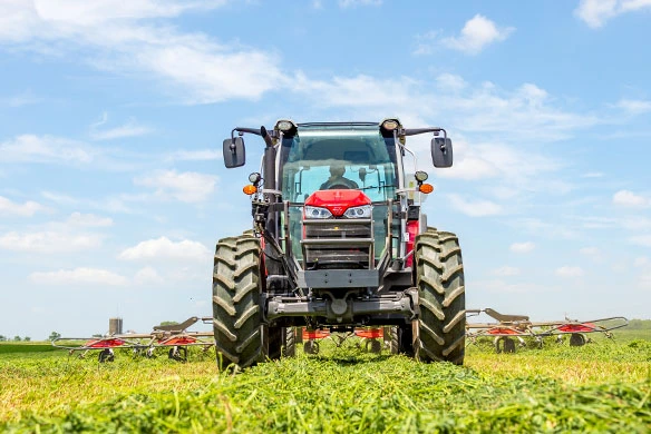Front view of Massey Ferguson 5M utility tractor operating in a hayfield with hay equipment attached.