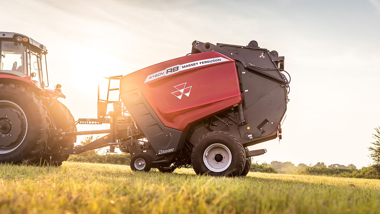 Hesston by Massey Ferguson 1 Series round baler in field at sunrise, hitched to tractor, ready for hay baling.