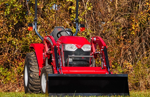 Front view of Massey Ferguson 1M Series compact tractor with front loader, displayed on green grass in a wooded area.