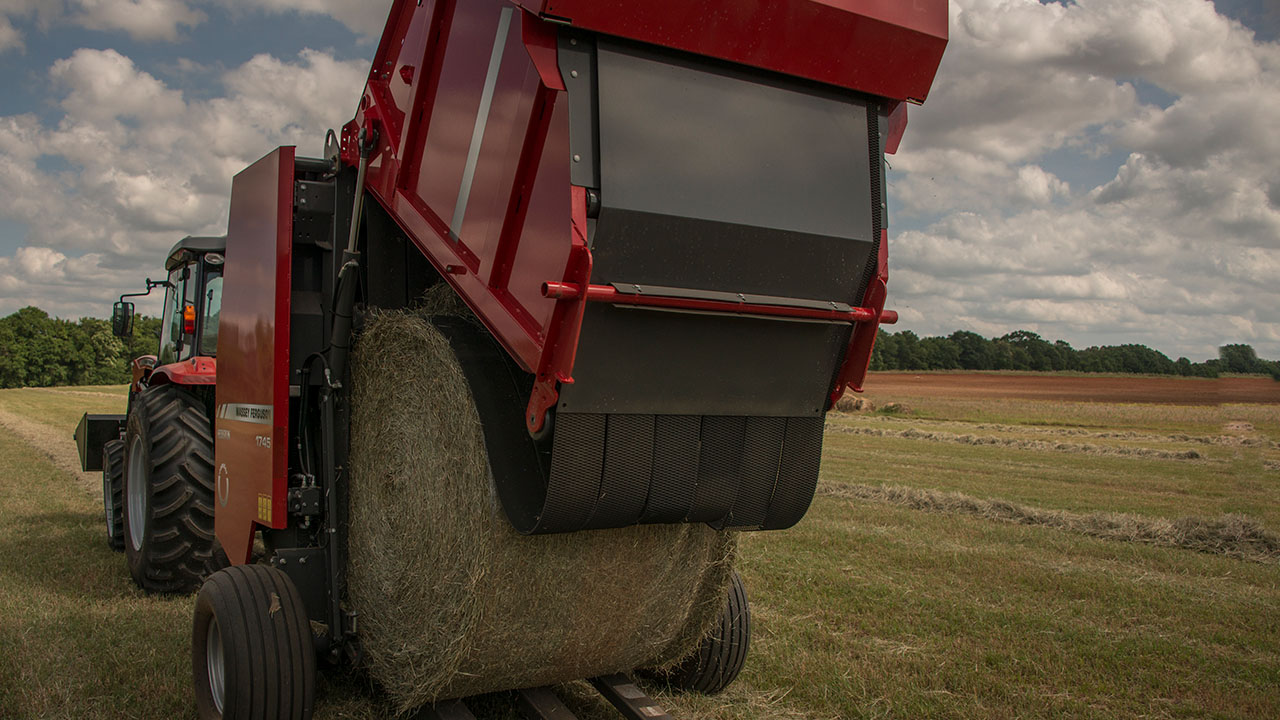 Hesston by Massey Ferguson 1700 Series round baler unloading hay bale in field, designed for efficient small farm baling operations.