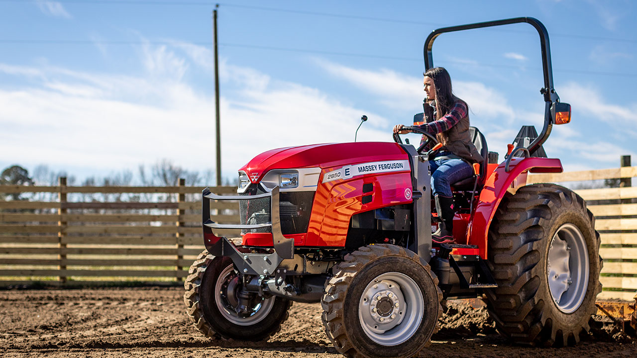 Woman operating Massey Ferguson 2800E Series compact tractor in horse pasture, ideal for farm chores.