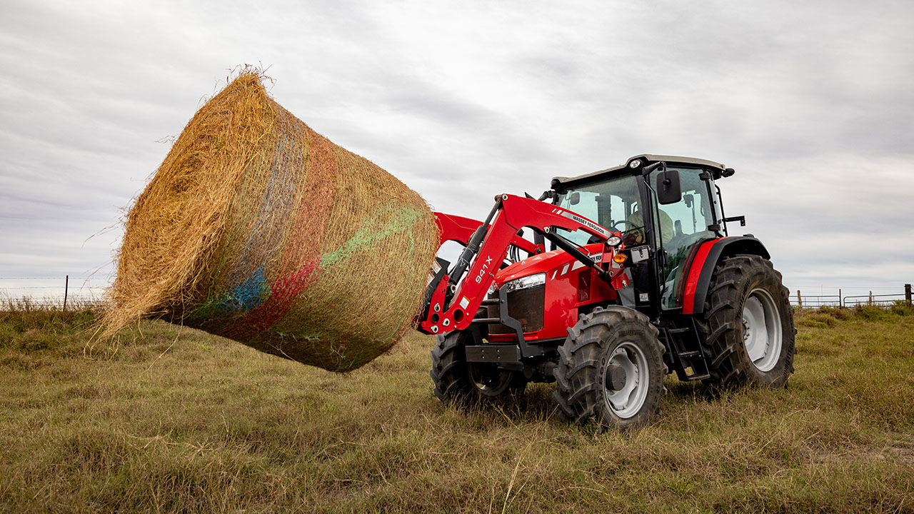 Massey Ferguson 5700 Series tractor lifting large round hay bale in field, ideal for livestock and hay operations.