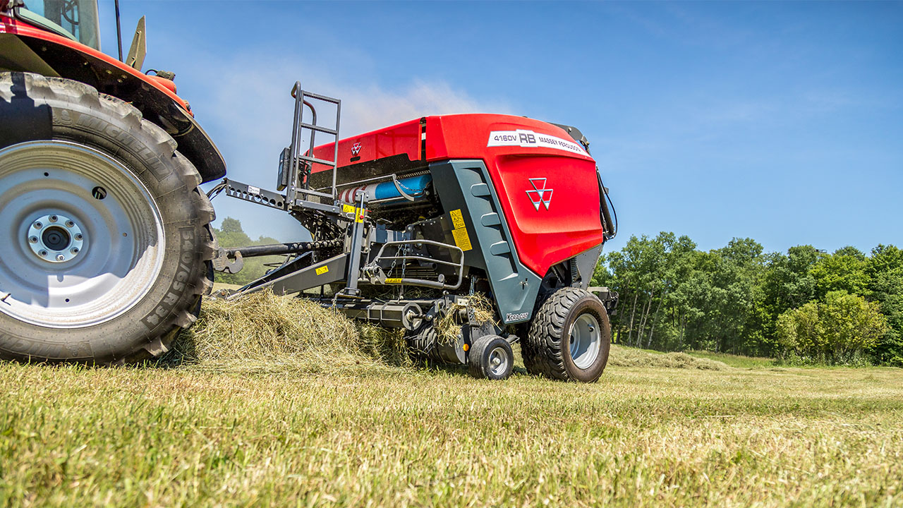 Hesston by Massey Ferguson RB 4160V picking up hay in field, attached to tractor, under clear blue sky.