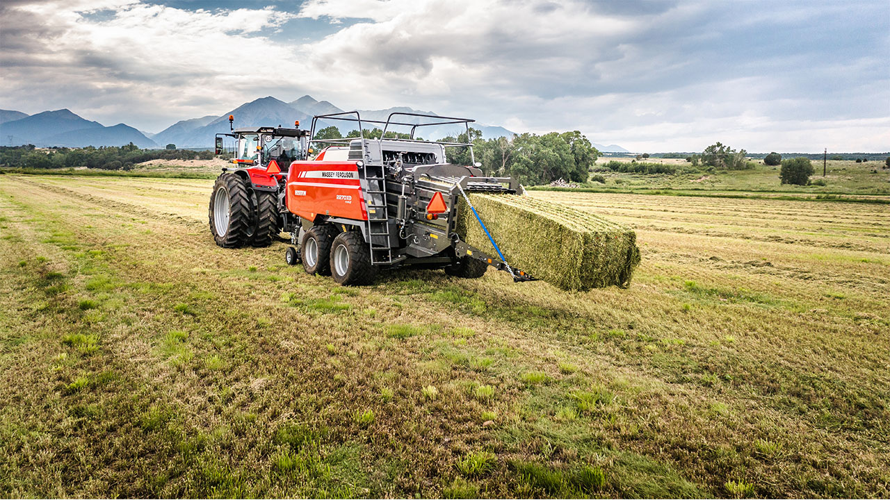 Hesston by Massey Ferguson LB2200 Series large square baler producing dense hay bale in open field with mountains in background.