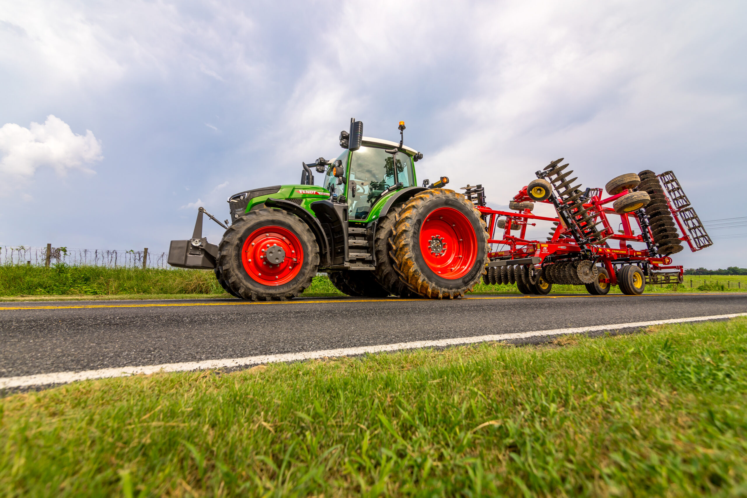 Fendt 600 Vario tractor transporting Sunflower tillage equipment on a country road under a cloudy sky.